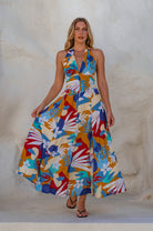 Woman wearing a multi-colored soft rayon patterned maxi dress with halter neckline, smocked back, and fitted bodice, in front of white background, front view