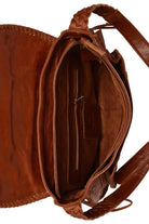 Close-up of the interior of a brown leather shoulder bag, showing the zippered compartment, interior pocket, braided strap, and stitched edge on a white background.
