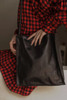 Person wearing a red and black checkered outfit holding a black leather bag.