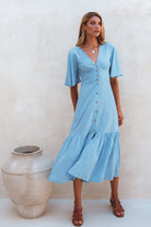 Woman wearing blue midi dress in a button-down silhouette with a smocked back and fitted front, tiered skirt, and butterfly sleeves standing against a neutral background, front view