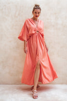 Woman wearing a coral maxi dress against a beige background, front view