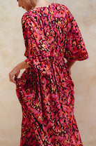 Woman wearing a vibrant, patterned dress with a neutral background, back view