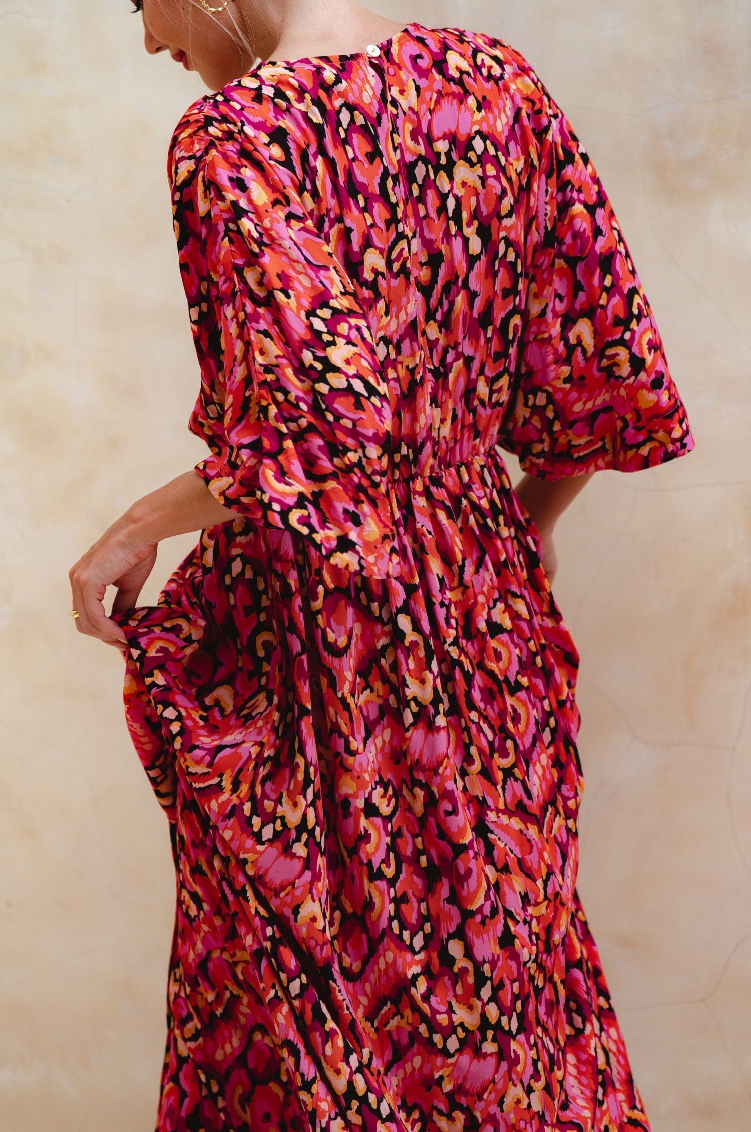 Woman wearing a vibrant, patterned dress with a neutral background, back view