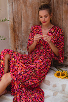 Woman in a vibrant, patterned dress sitting on stone steps with a wooden wall background.