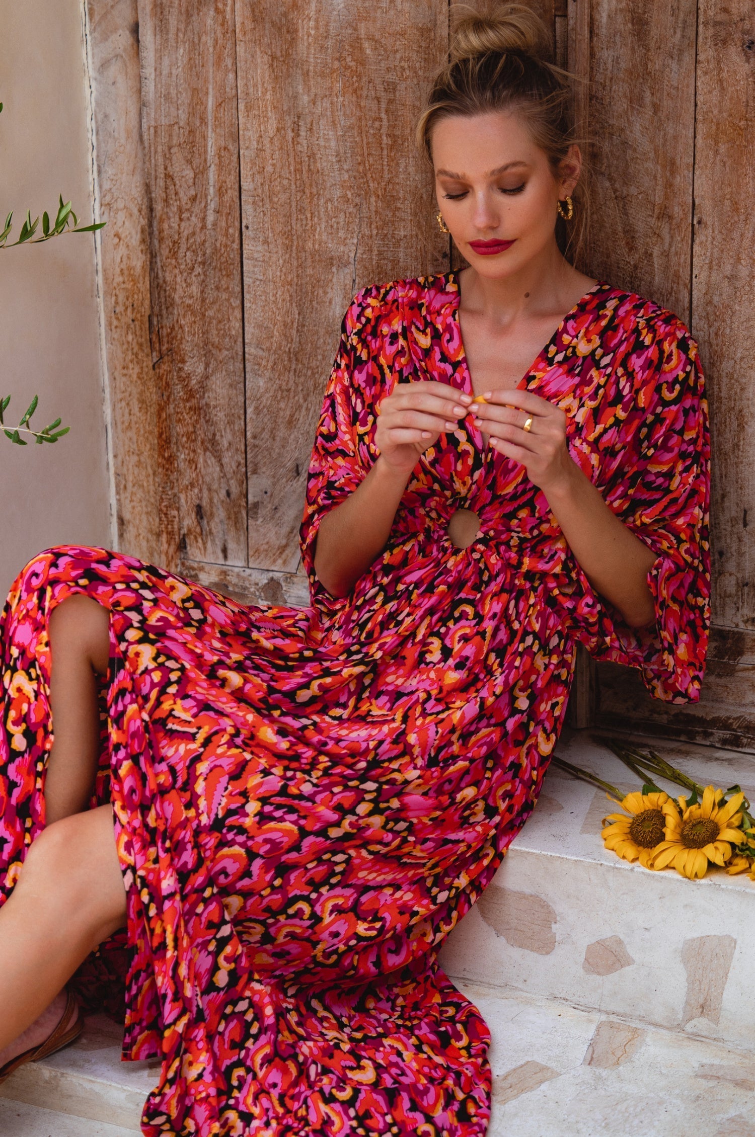 Woman in a vibrant, patterned dress sitting on stone steps with a wooden wall background.