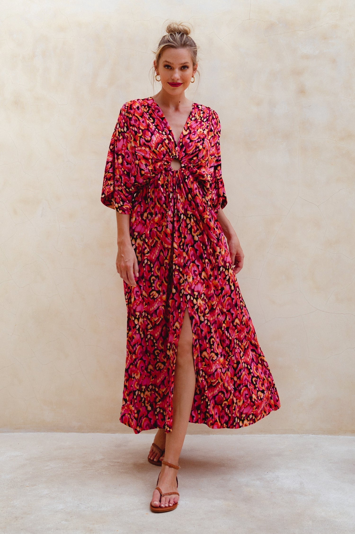 Woman wearing a red floral maxi dress against a beige background, front view