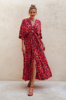 Woman wearing a red floral maxi dress against a beige background, front view