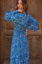 Woman wearing a blue floral dress standing against a wooden background