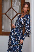 Woman wearing a navy blue floral dress standing by a window.