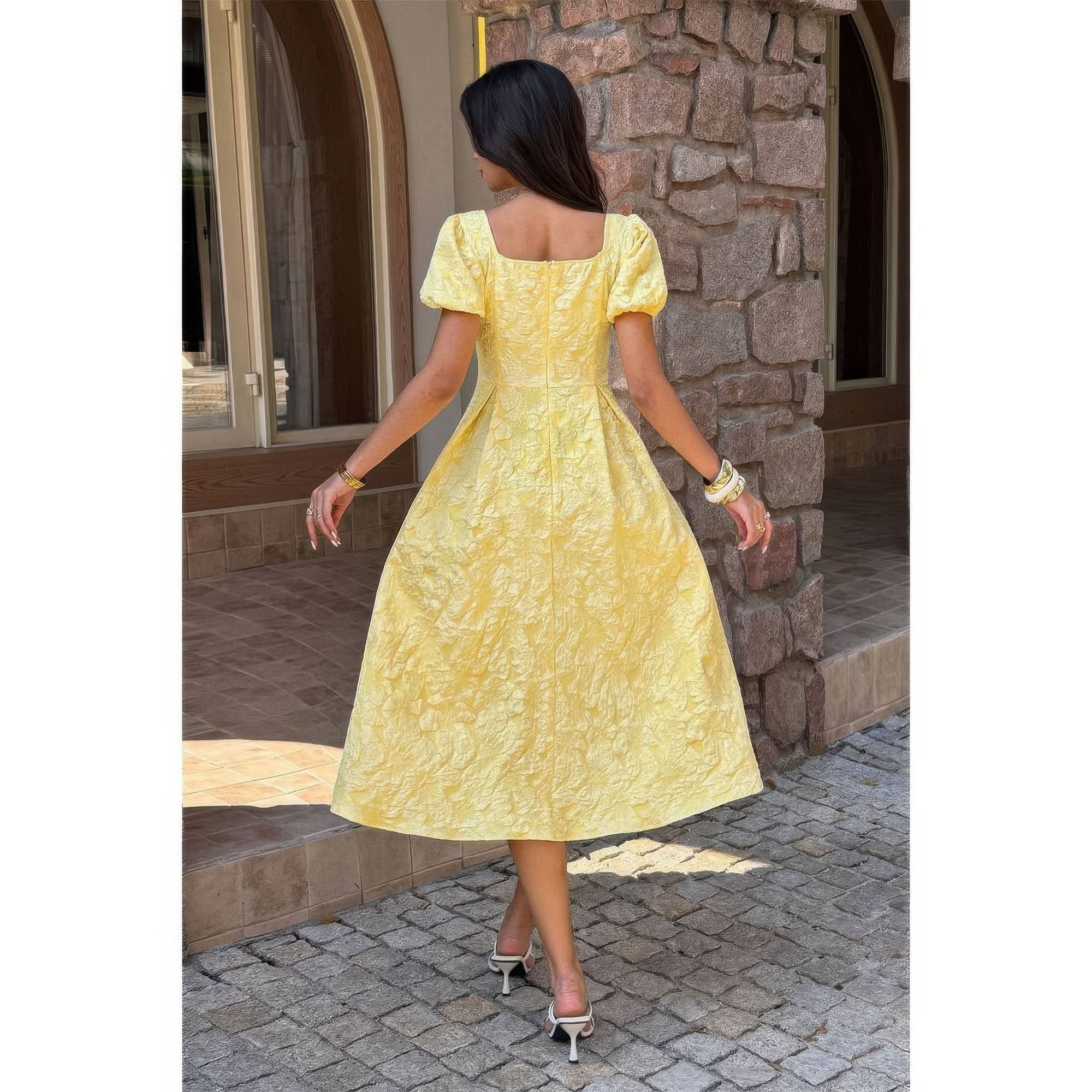 Woman in a yellow dress standing in front of a stone wall- back view.