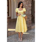 Woman in a yellow dress standing in front of a stone wall.