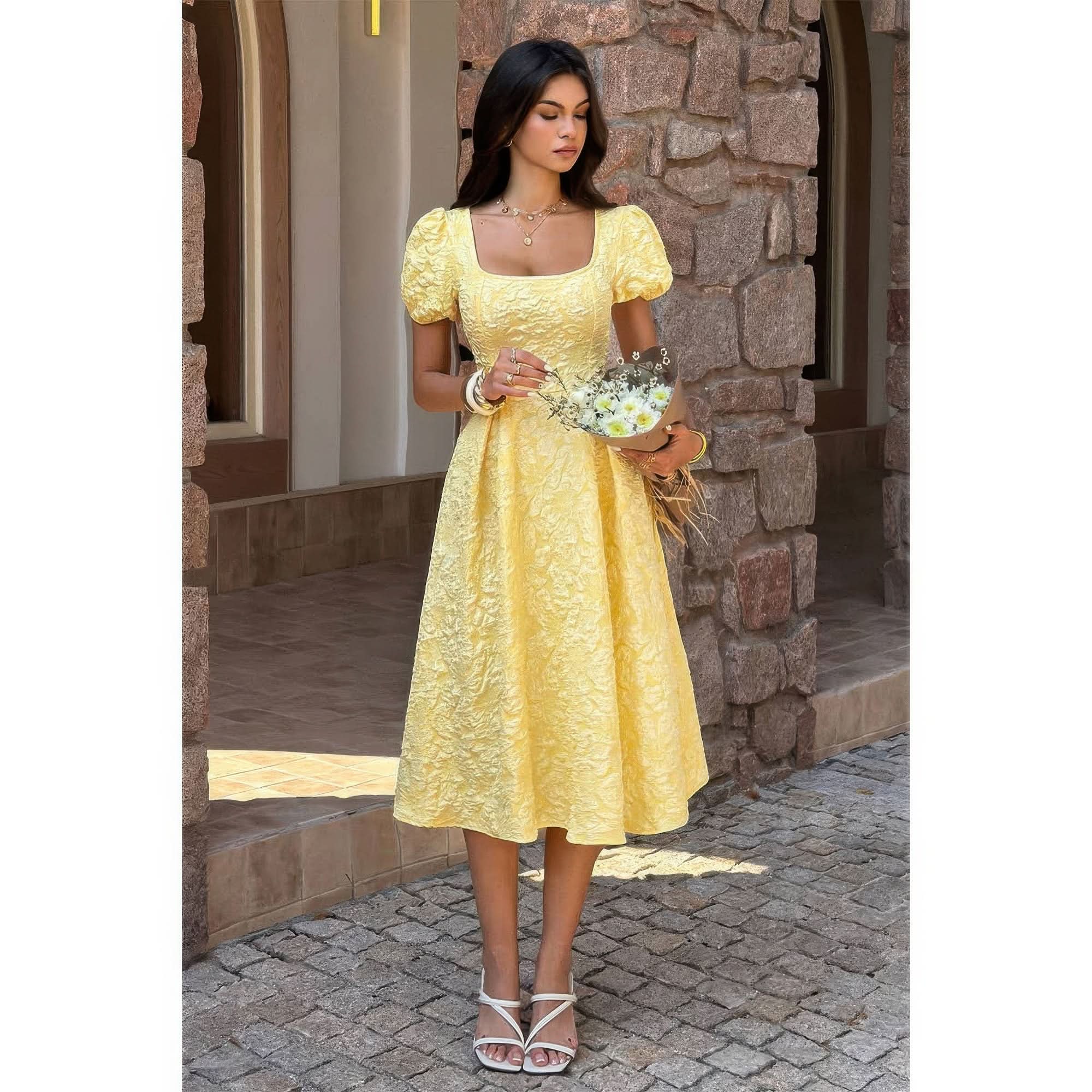 Woman in a yellow dress standing in front of a stone wall.