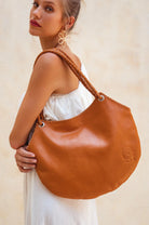 Woman carrying a camel leather handbag against a neutral background