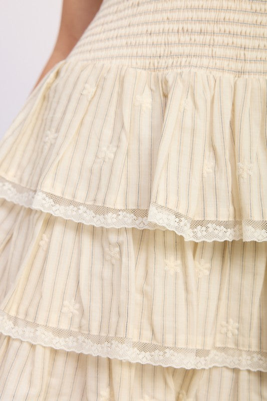 close up of woman wearing cream strapless smocked tiered mini dress front view on white background