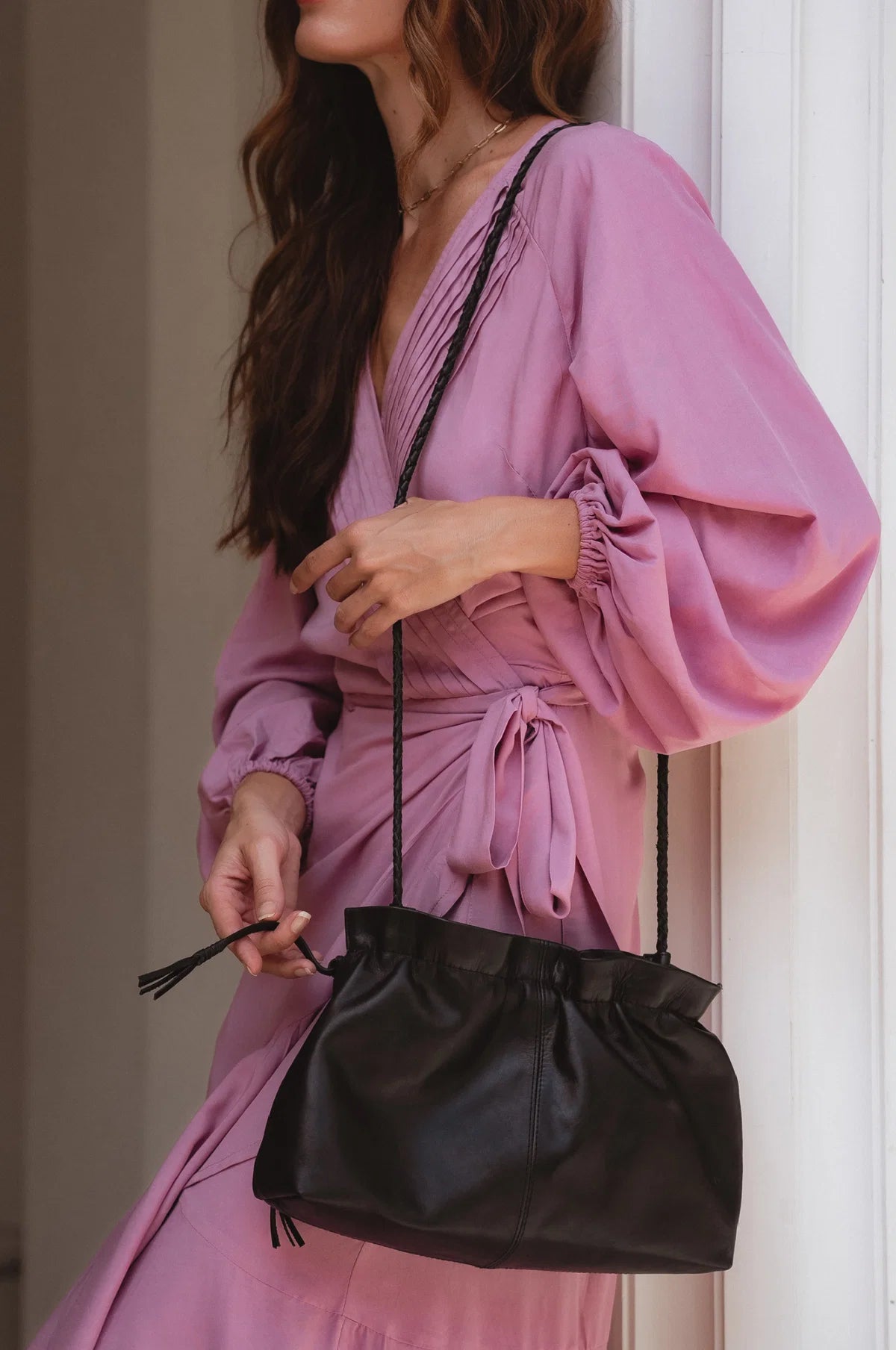 Woman in a pink dress holding a black leather handbag indoors.