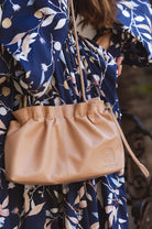 Beige leather handbag held by a person wearing a blue floral dress.
