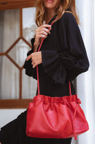 Person holding a red leather crossbody handbag with a blurred background
