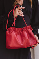 Red leather handbag with rope handles held by a person wearing a black outfit.