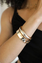 Close-up of woman wearing polished gold-tone bangle duo with a black top.