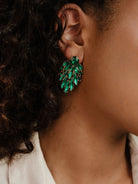 Close-up of woman wearing emerald-green crystal cluster earring against a dark background.