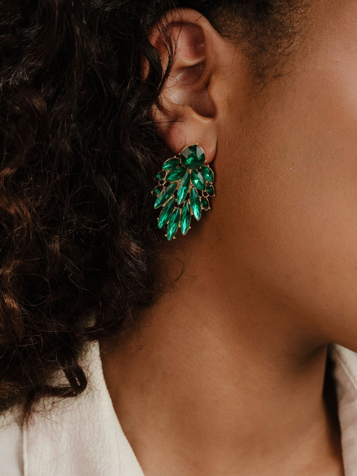 Close-up of woman wearing emerald-green crystal cluster earring against a dark background.
