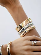 Woman wearing polished gold-tone bangle duo in a mixed-metal bracelet stack.