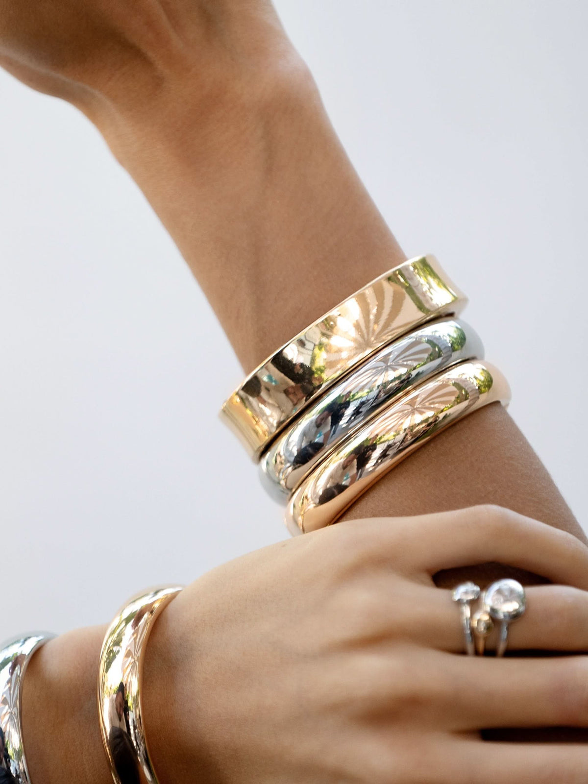 Woman wearing polished gold-tone bangle duo in a mixed-metal bracelet stack.