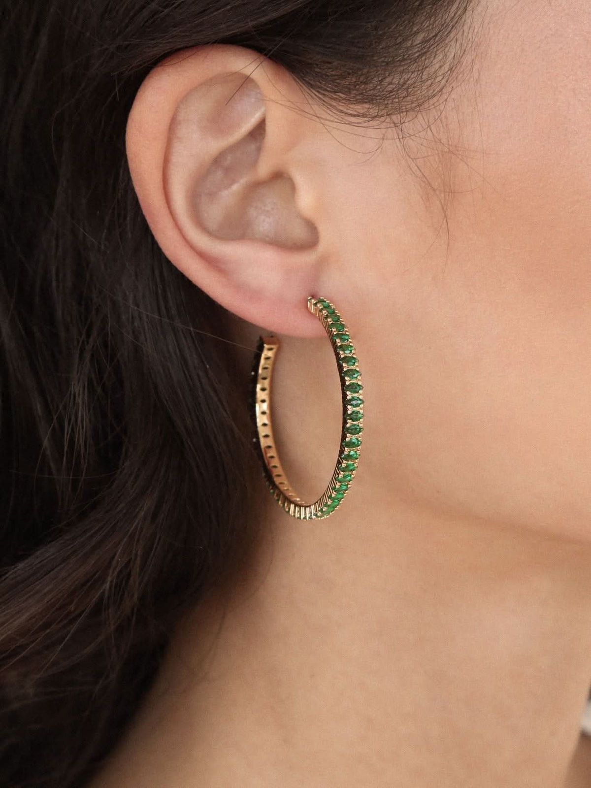 Woman wearing slim green marquise-style stone hoop earring against a neutral background.
