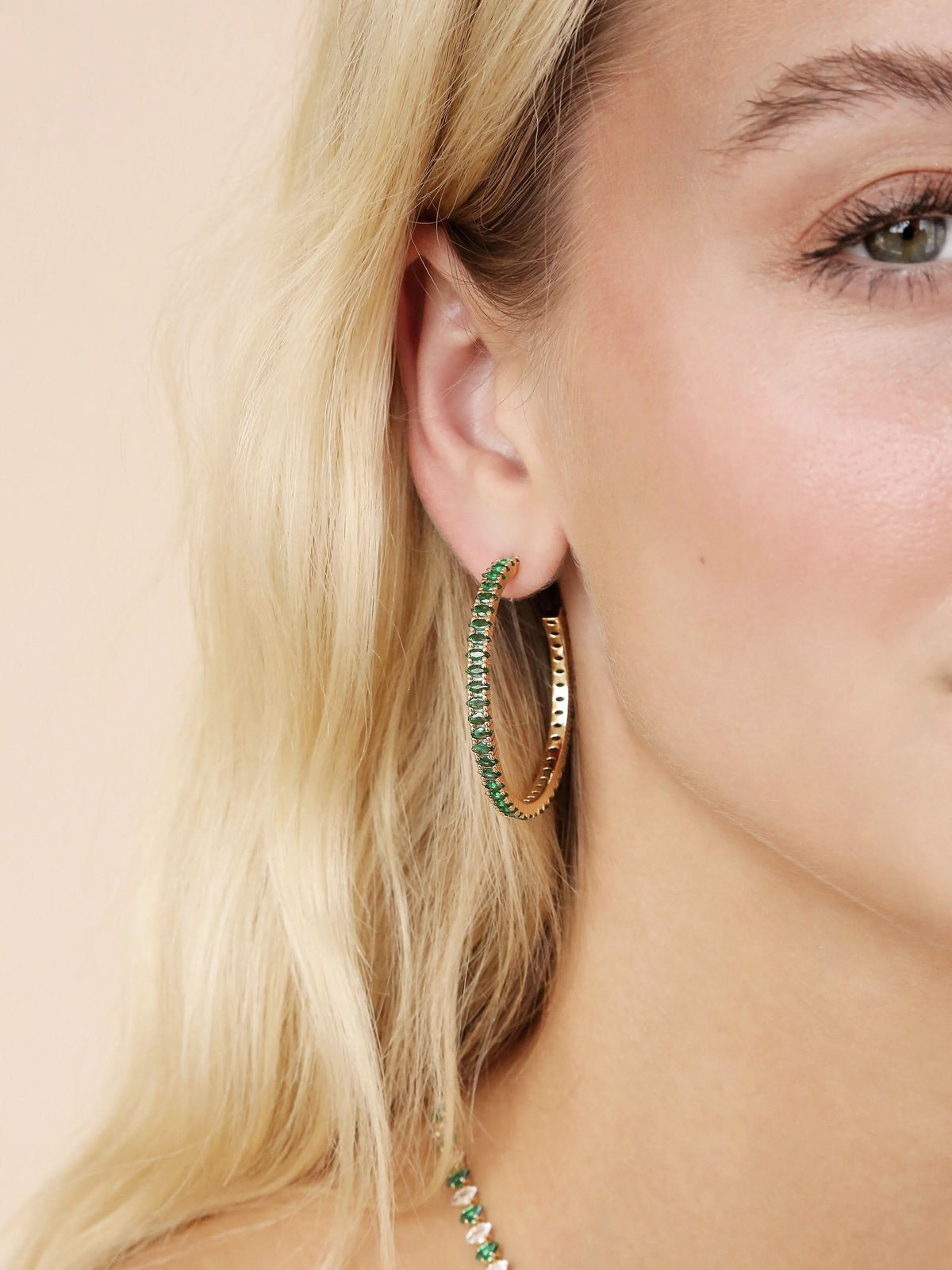 Woman wearing a green crystal hoop earring with gold-tone details indoors.