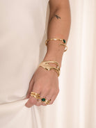 Woman wearing gold-tone crystal wrap ring and green-accented bracelets.