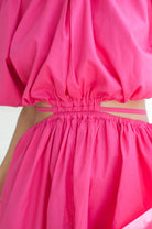 Close-up of a bright pink dress with cut-out design on a white background front view.
