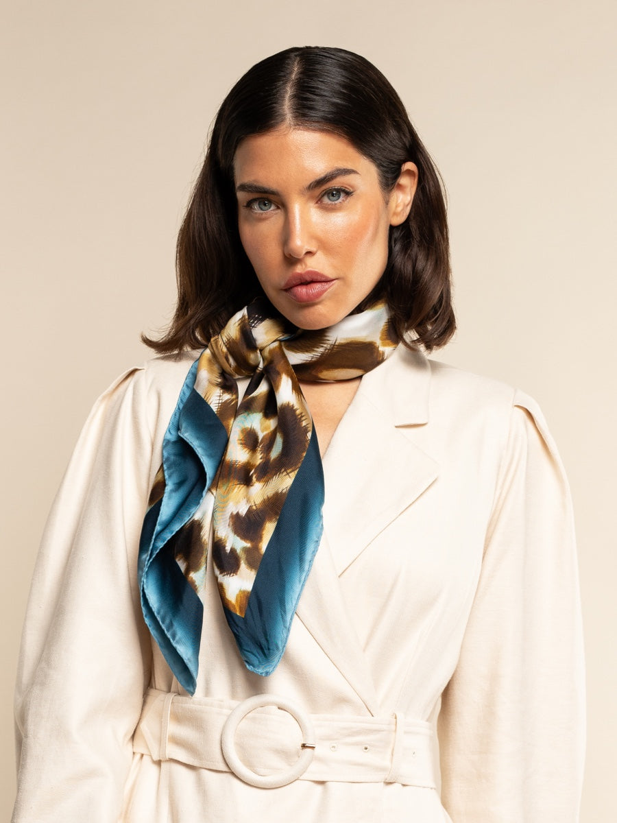Woman wearing a white coat and a patterned silk scarf with a blue border on a beige background