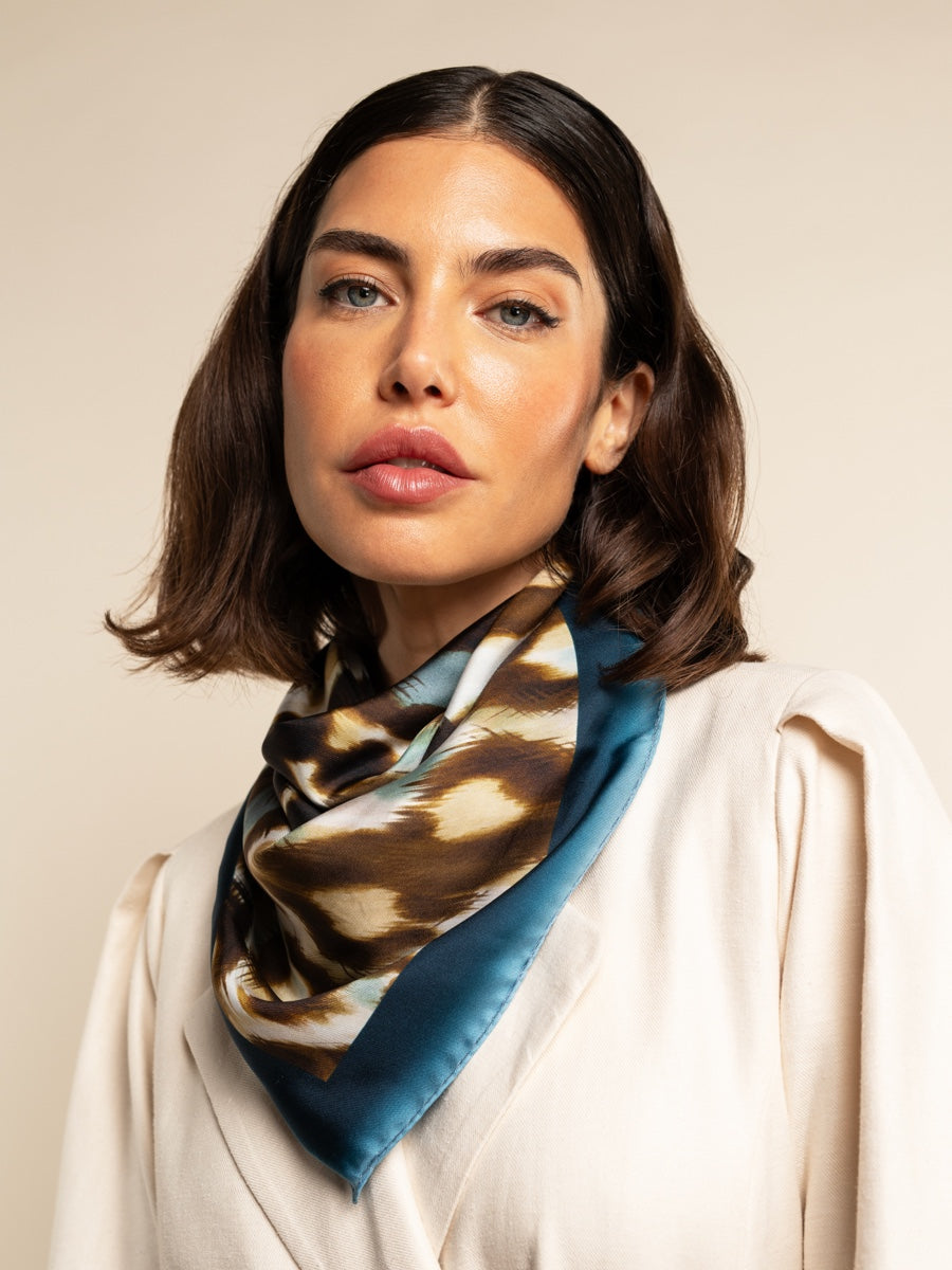 Woman wearing a patterned silk scarf on a beige background