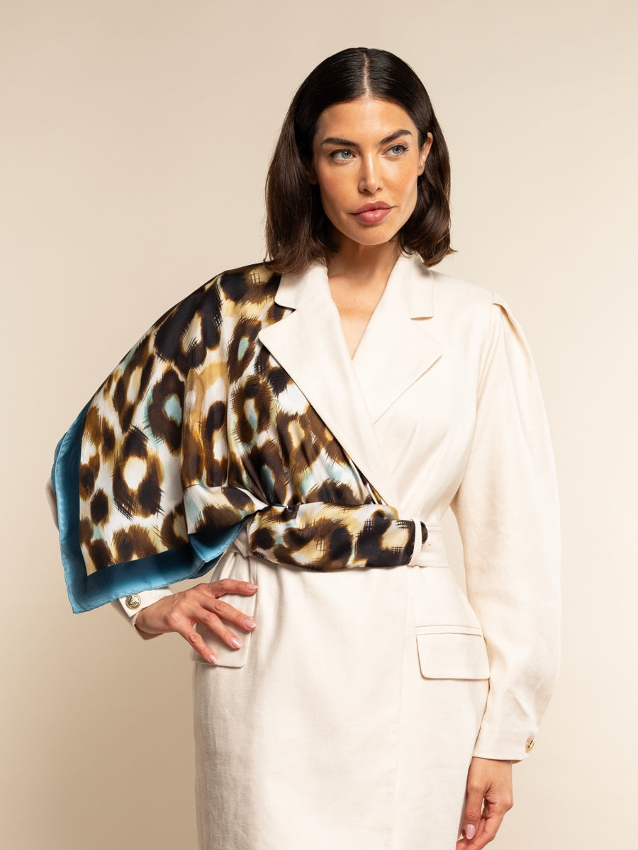 Woman wearing a white blazer with a leopard print and blue velvet scarf.