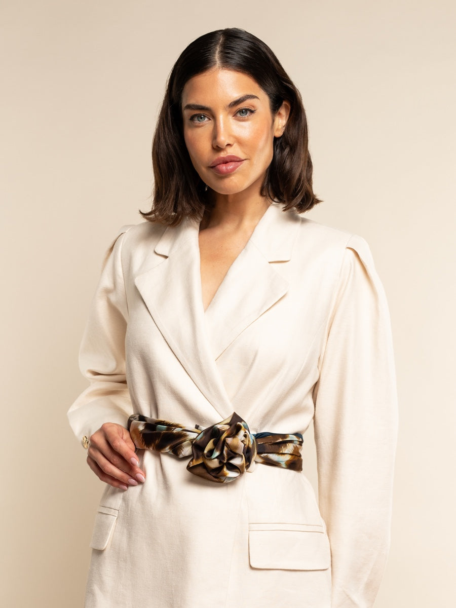 Woman wearing a white blazer with a leopard print silk scarf as a belt against a beige background