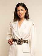Woman wearing a white blazer with a leopard print silk scarf as a belt against a beige background