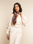 Woman wearing a beige suit with a patterned scarf against a plain background