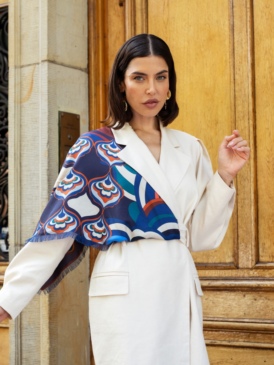 Woman wearing a colorful silk scarf and white outfit in front of a wooden door.