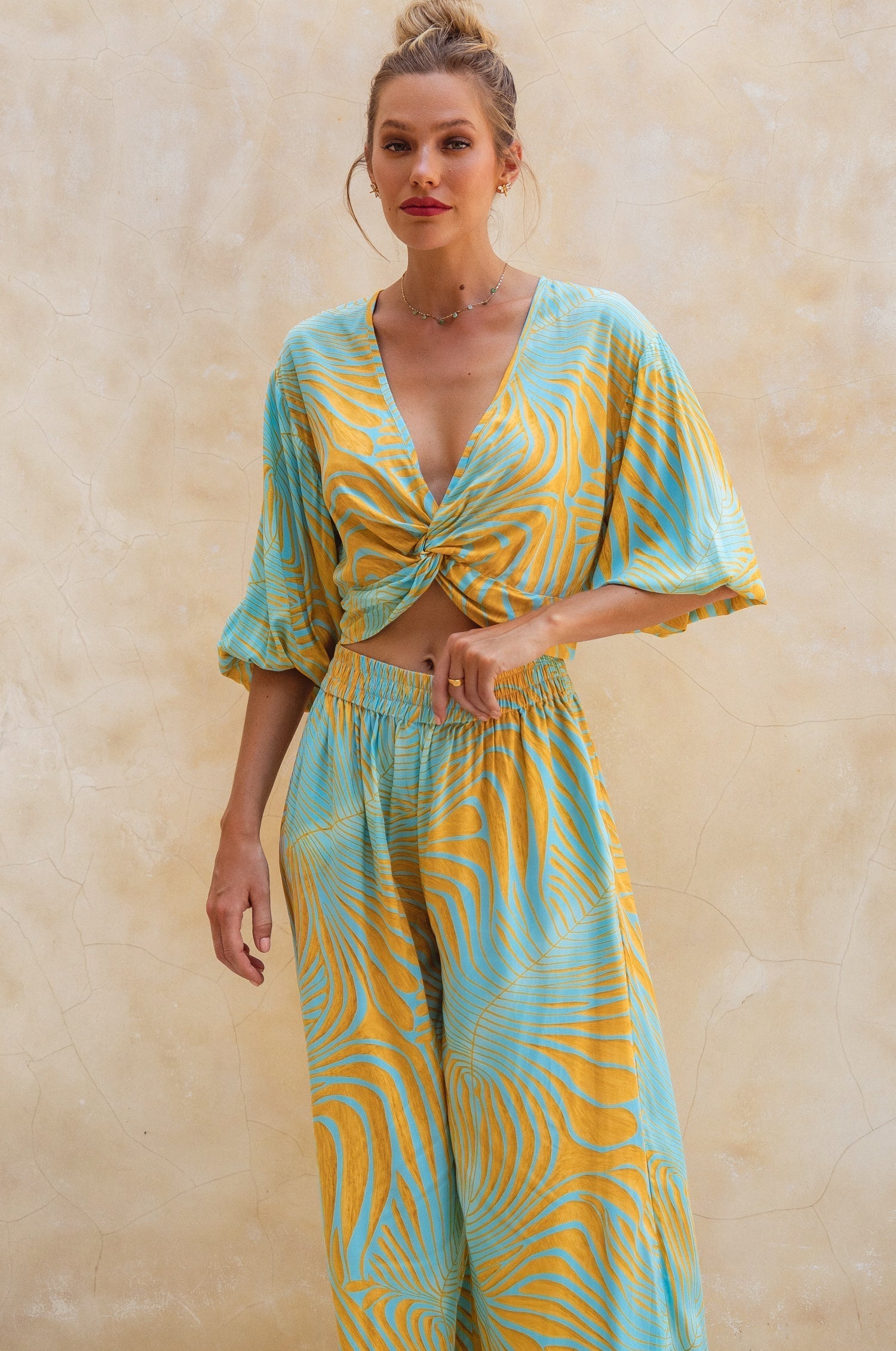 Woman wearing a yellow and blue patterned outfit against a beige wall