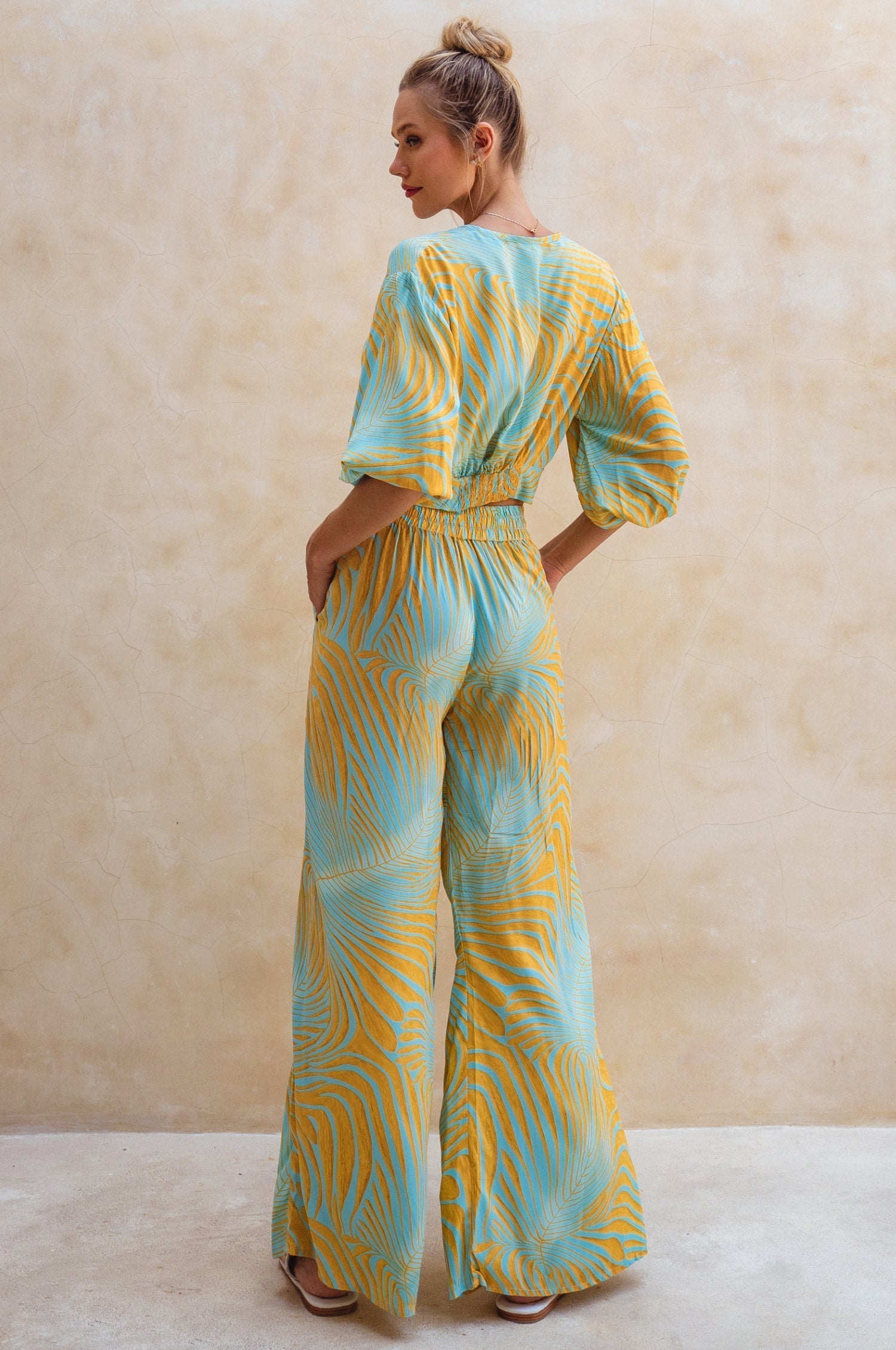 Woman wearing a blue and yellow patterned jumpsuit against a beige background