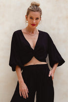 Woman wearing a black unlined slip-on cropped style top with twisted detailing on the front and elasticated sleeves and matching pants against a plain background