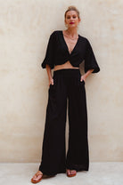 Woman wearing a black outfit with wide-leg pants against a beige background