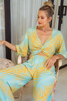 Woman wearing a yellow and blow patterned slip-on cropped style top with twisted detailing on the front and elasticated sleeves and matching pants sitting on a chair.