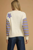 Back of cream floral knit sweater with small lavender flower on shoulder, striped sleeves and ribbed hem.