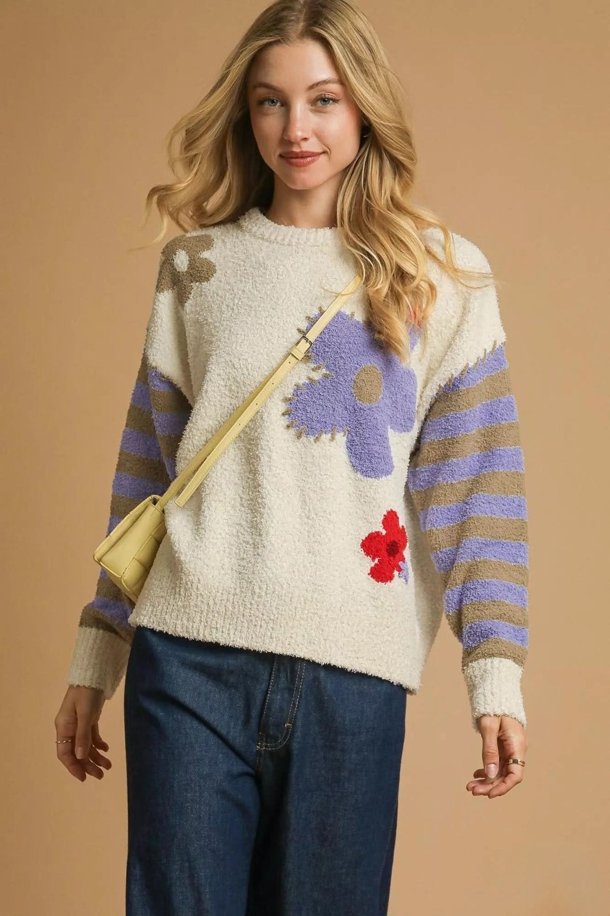 Flower Child Cozy Knit Sweater in cream with lavender floral designs, taupe and lavender striped sleeves, styled with dark denim jeans.