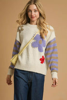 Flower Child Cozy Knit Sweater in cream with lavender floral designs, taupe and lavender striped sleeves, styled with dark denim jeans.