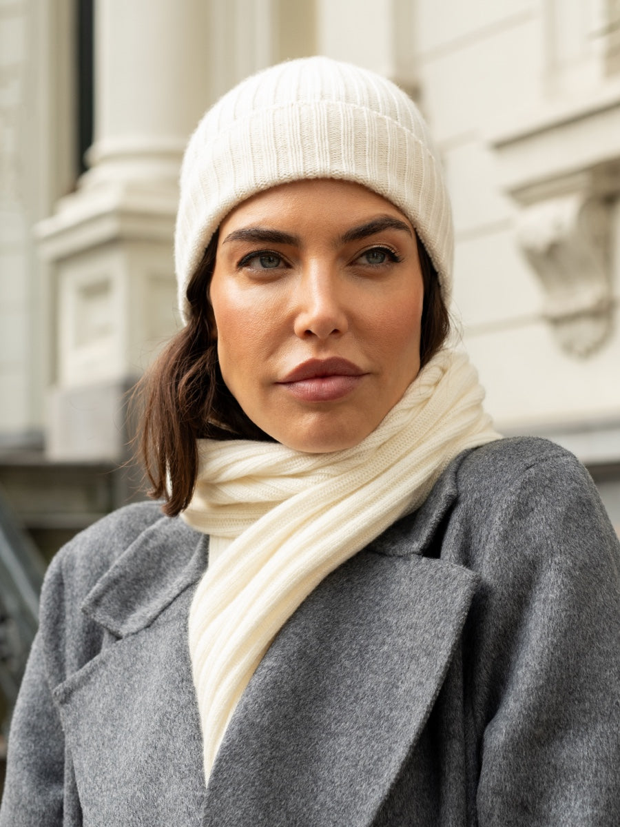 Woman wearing an ivory cashmere knit beanie and scarf with a gray coat outdoors.