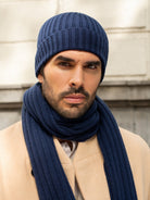 Man wearing a blue knit hat and scarf against a neutral background