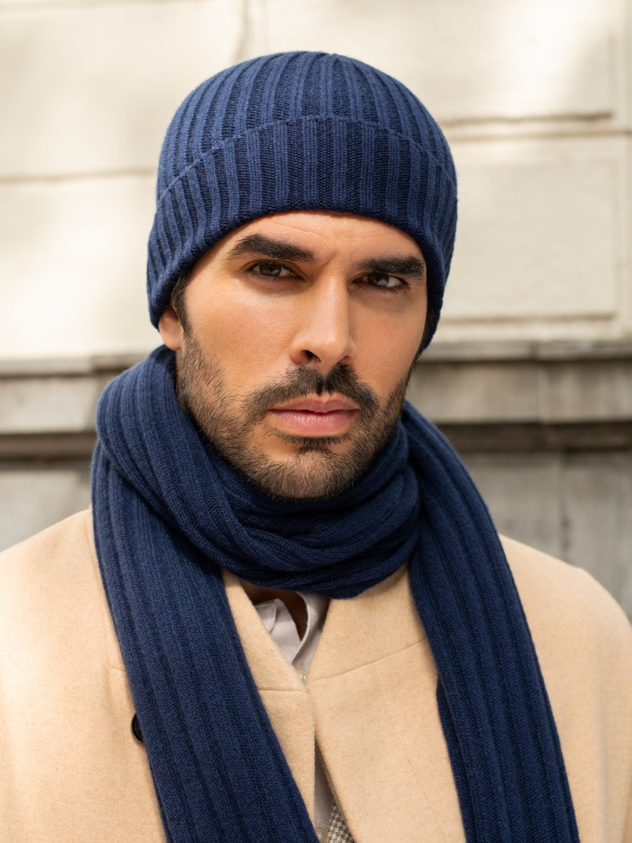 Man wearing a blue knit hat and scarf against a neutral background