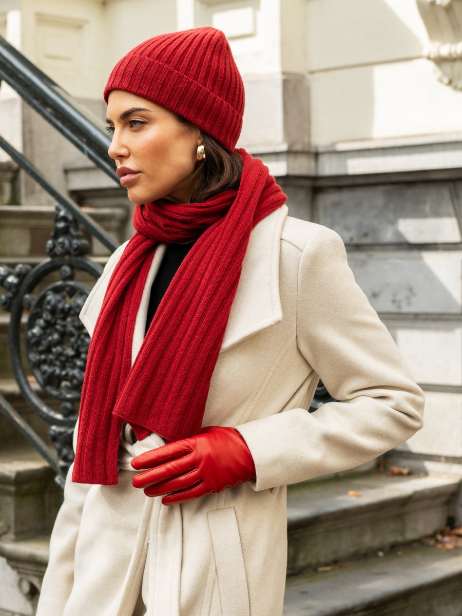 Person wearing a red cashmere beanie, scarf, and gloves standing on steps.